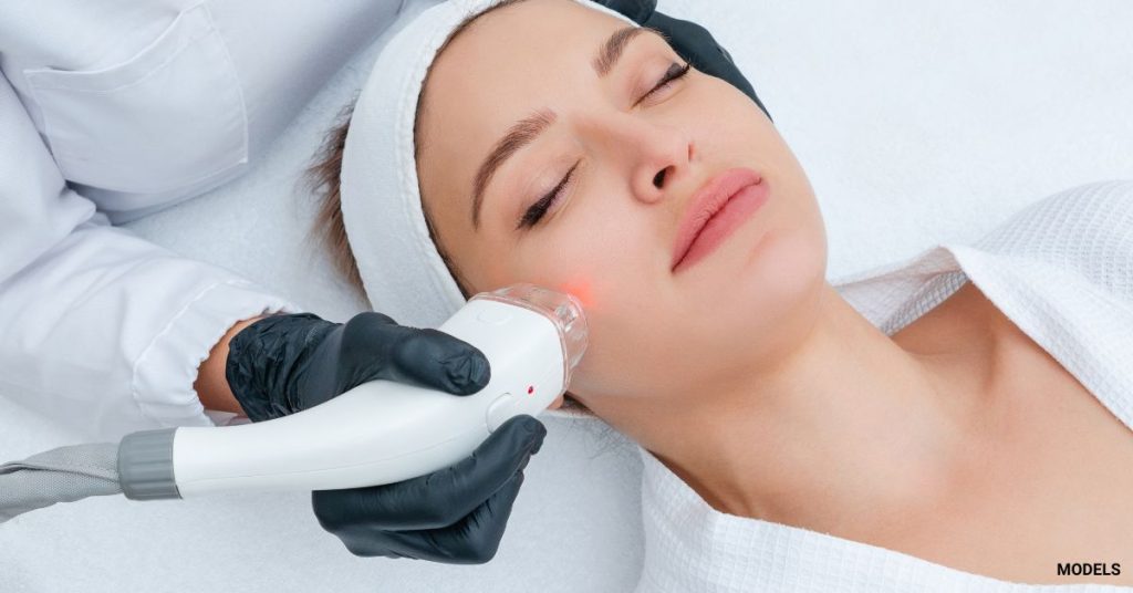 Woman with clear glowing skin is getting a laser treatment on her face from a provider. (Models)