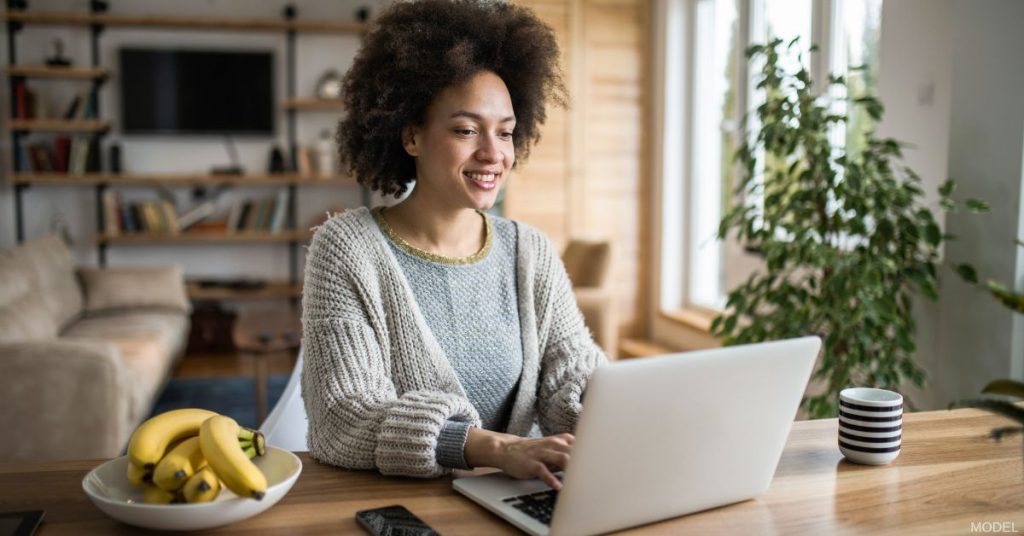 Woman sitting at the table look at her laptop. (model)